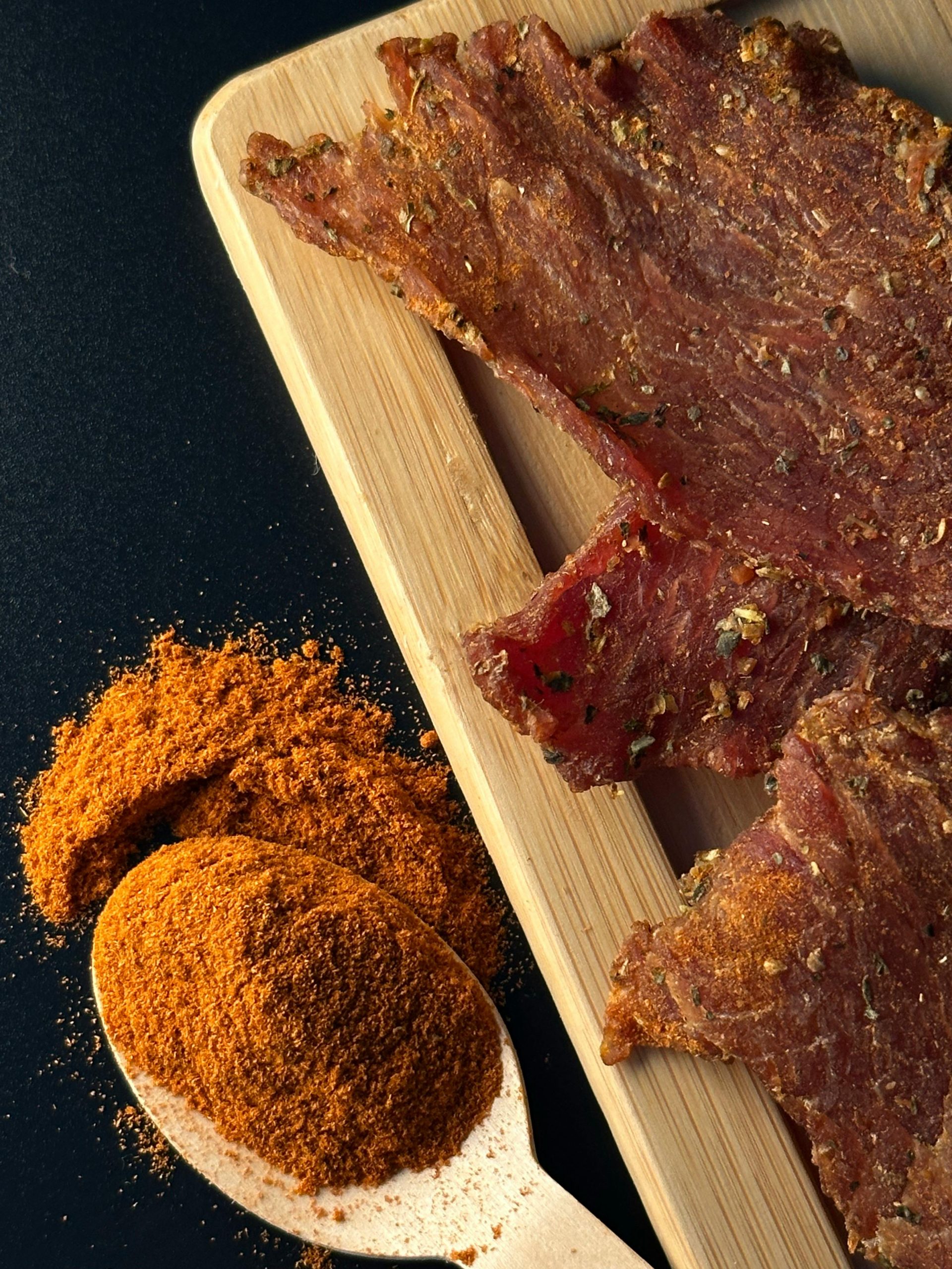 Close-up of savory beef jerky slices with a spicy powder on a wooden spoon creating a flavorful combination.